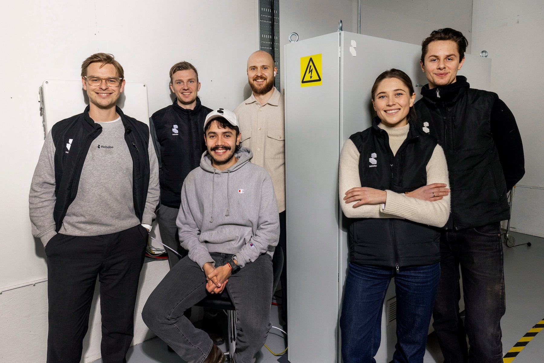 Sex av Rebabas &aring;tta medarbetare st&aring;ende vid ett av f&ouml;retagets batterilager. Till h&ouml;ger st&aring;r grundarna Paula Runsten och Felix Kruse.